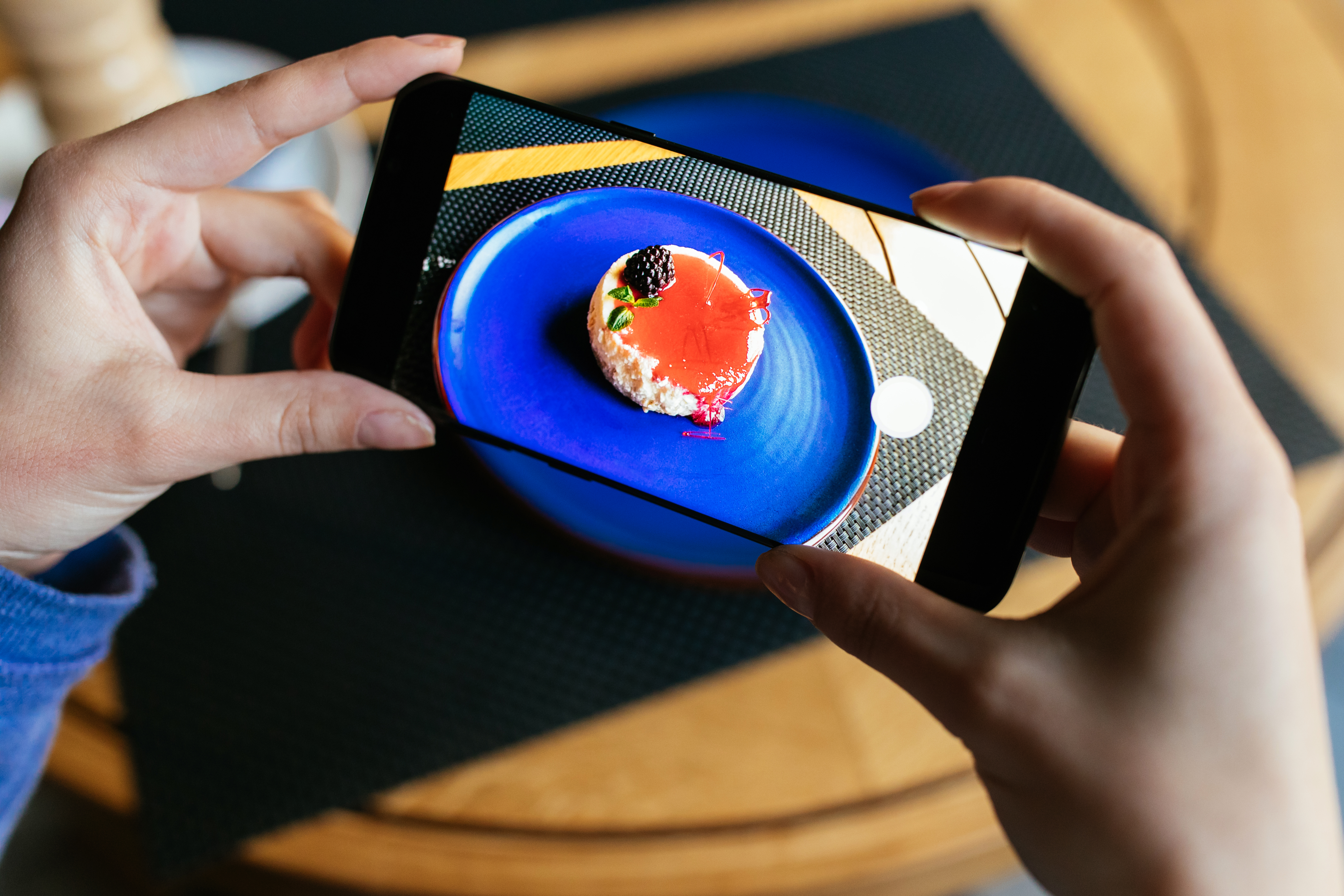 Mains photographiant un plat gastronomique avec un smartphone